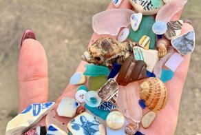 Девушка ищет на пляже материалы для творчества и показывает находки