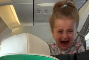 Плачущий ребенок выглянул из-за сиденья самолета