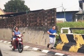 В Малайзии женщина на мотоцикле и с палкой в руках заставляет бегать своего полного сына