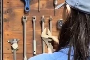 Девушка пытается повесить разводной ключ на стену
