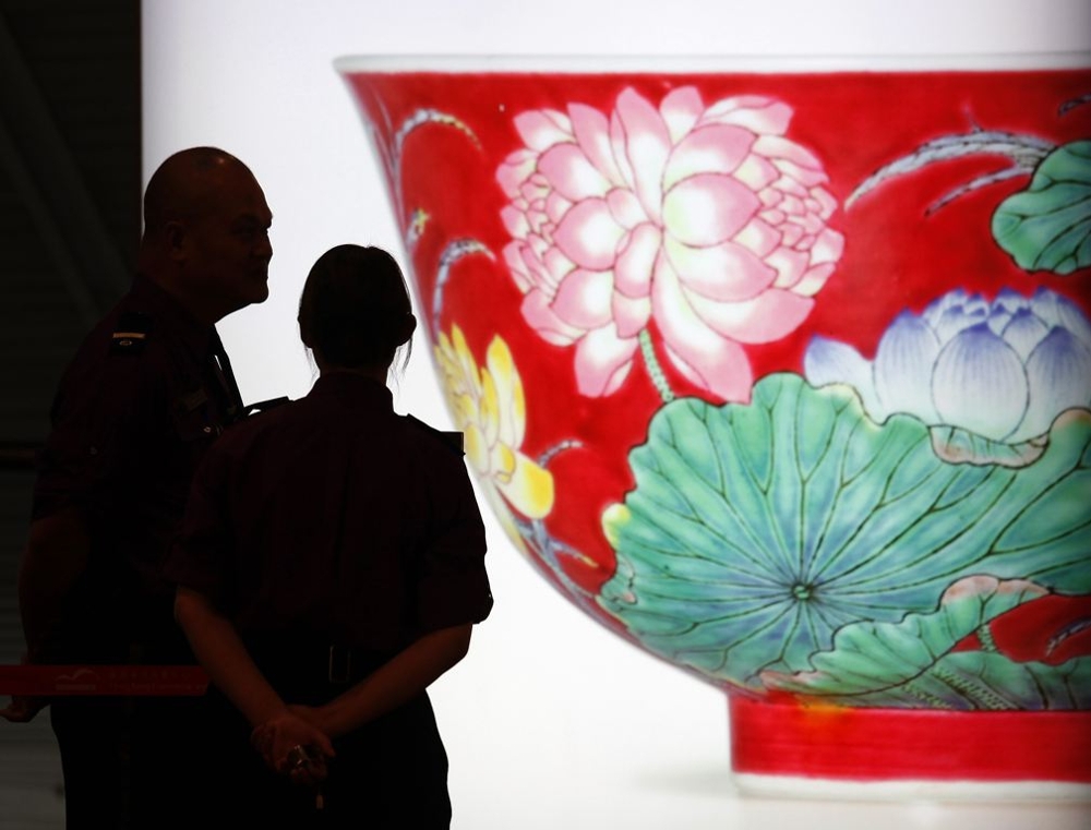 Security guards chat in front of a light box featuring a photograph of a magnificent Ruby-Ground Falangcai "Double-Lotus