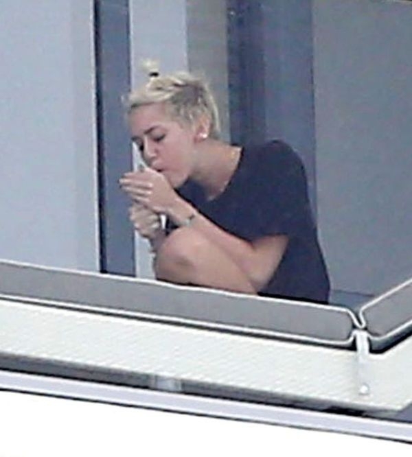 Miley Cyrus lighting up a hand-rolled cigarette on the balcony