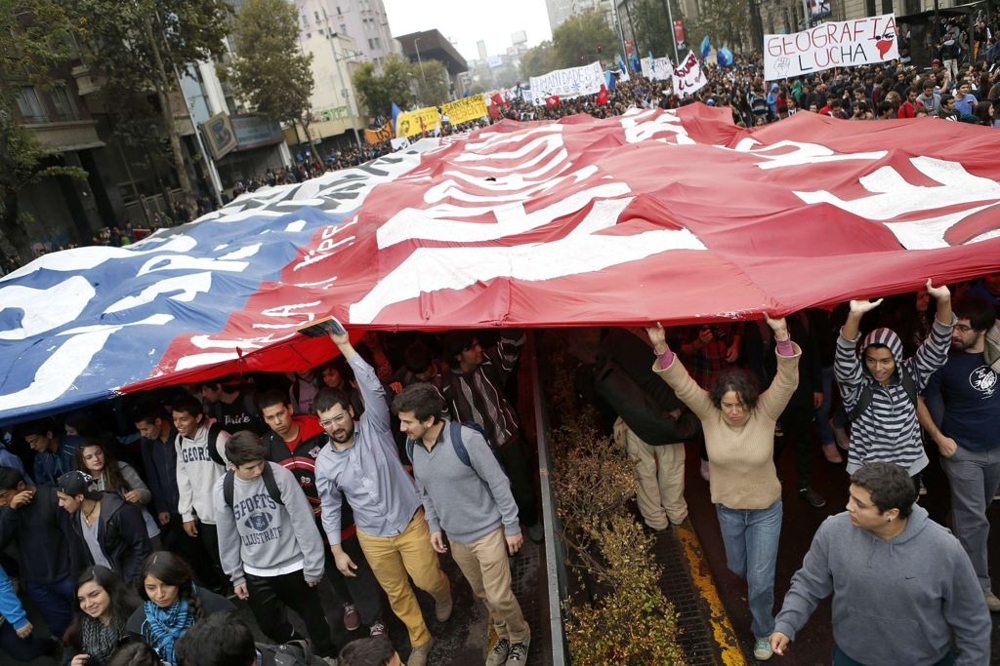 Student protesters march as they hold a huge Chilean flag