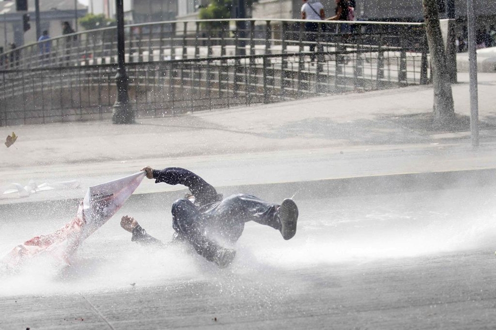 A student protester is hit by a jet of water released from a riot police water cannon