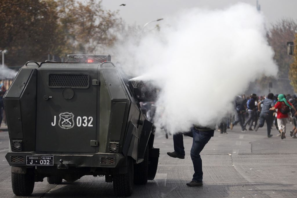 A student protester is covered by a tear gas cloud from a police vehicle