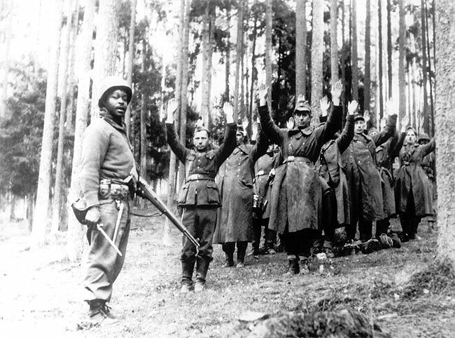 African American soldier looks pleased to guard captured Nazi German soldiers. April 1945