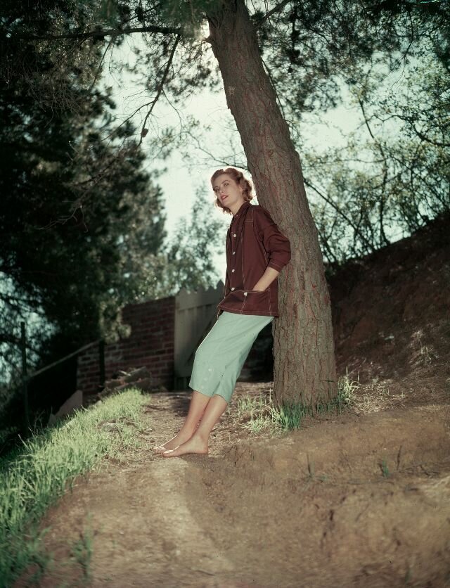 1953. Walking though the forest, Kelly leans against a tree barefoot for a photoshoot around her home.