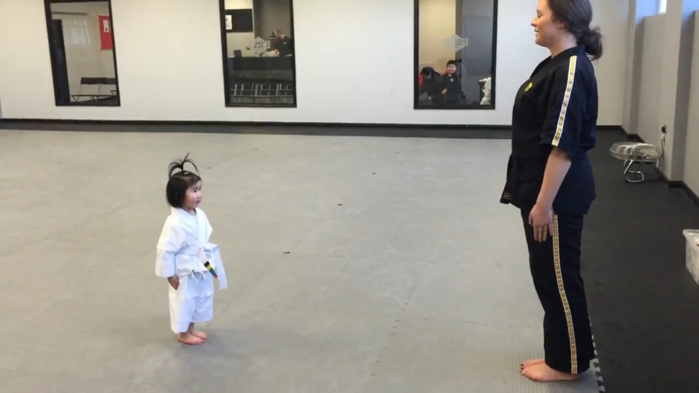 Трехлетняя девочка повторяет слова и движения своего тренера по тхэквондо 
