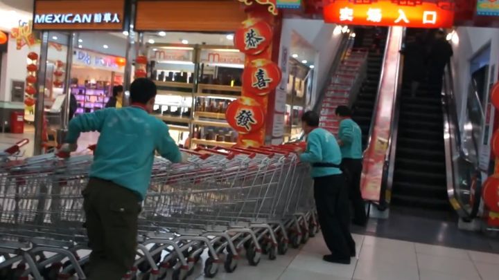 Сотрудники китайского супермаркета поднимают тележки на эскалаторе 