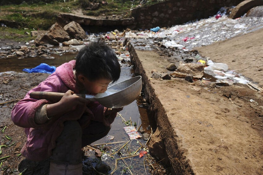 11. Ребёнок пьёт воду из грязного ручья в Фуюань, провинция Юньнань