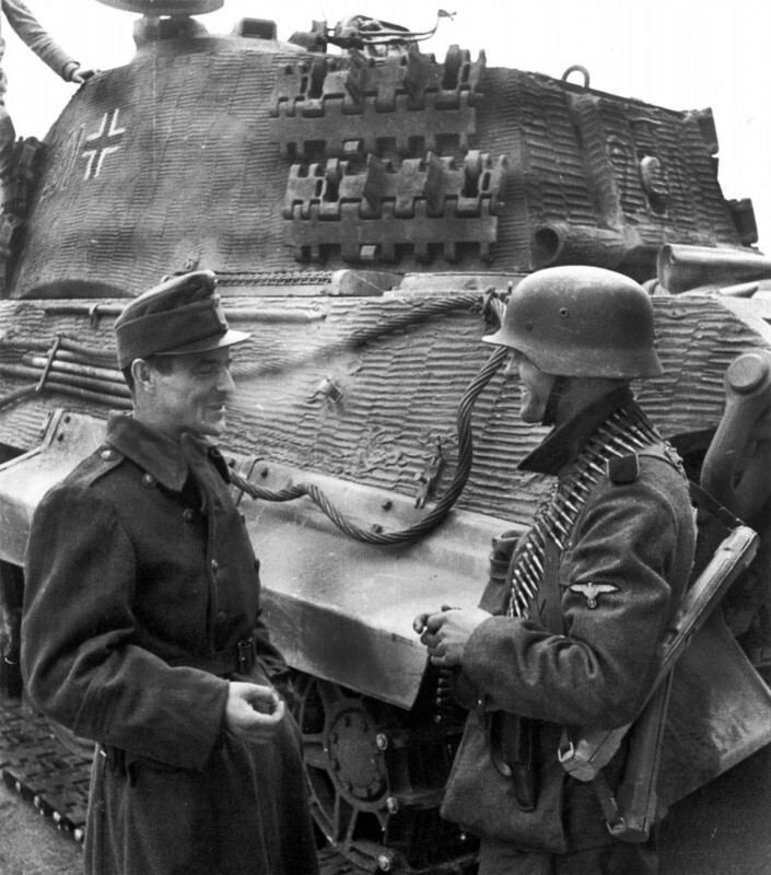 Венгерский солдат курит вместе с членом пулеметного расчета части СС у танка Pz.Kpfw. VI Ausf. B «Тигр II». Венгрия. Конец декабря 1944 года.
