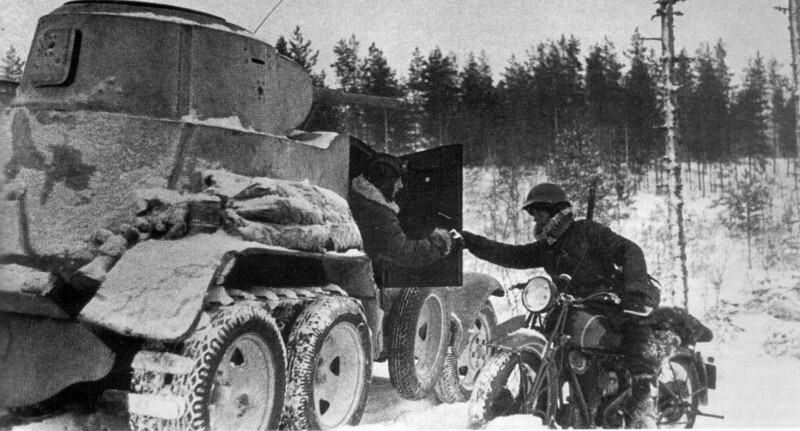 Вестовой на мотоцикле передает сообщение экипажу советского бронеавтомобиля БА-10. Задние колеса машины обуты в сьемные гусеничные цепи типа «Оверолл».  Карельский перешеек.