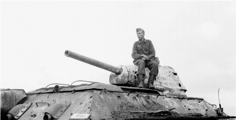Немецкий солдат позирует, сидя на башне подбитого в поле советского танка Т-34. По характерным признакам машина выпуска апреля 1943 года и производства завода №112 «Красное Сормово». 