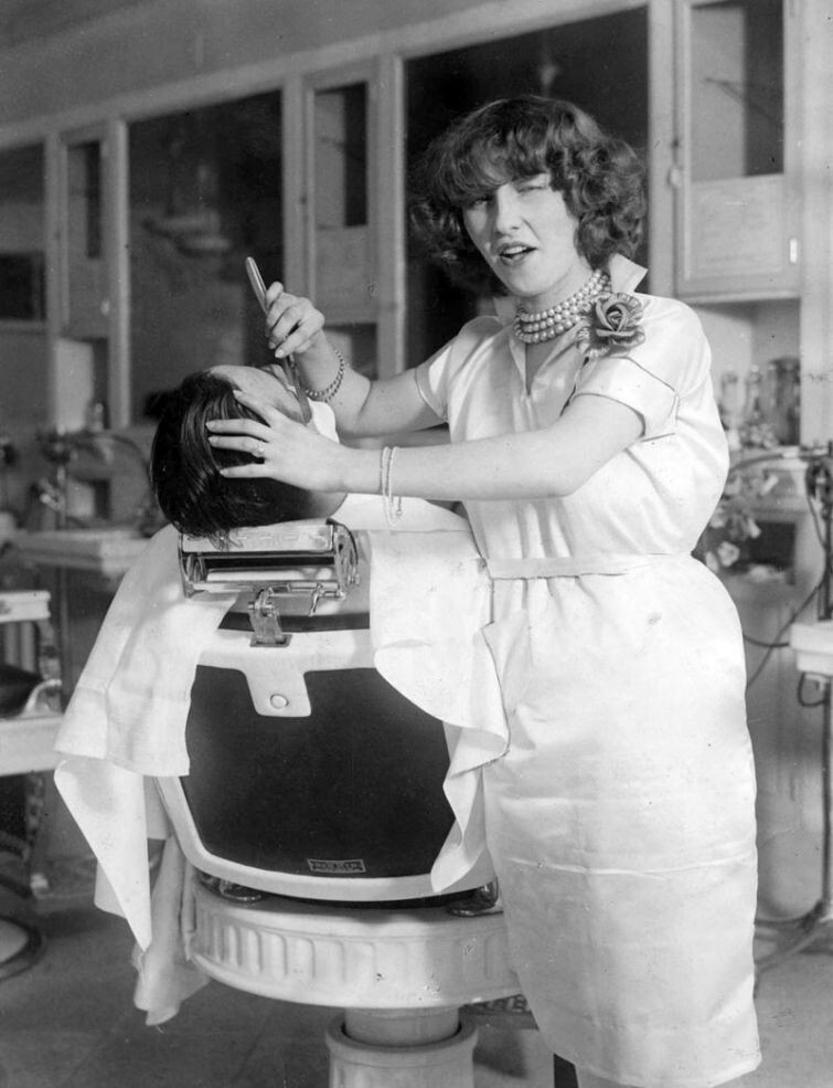 Первая лицензированная женщина парикмахер Нью-Йорка мисс Джин Деверо позирует фотографу во время бритья клиента, 1927 год