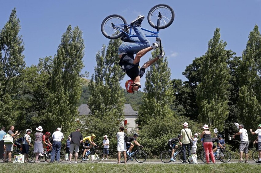 Пелотон велогонщиков проезжает мимо ВМХ-райдера, которые исполняет трюки, на 10-м этапе велогонки «Тур де Франс»