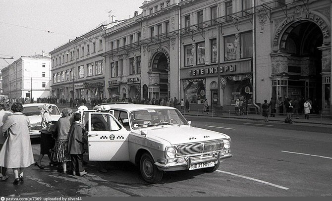 В Петровский пассаж сбегаются люди. А на переднем плане в такси садятся цыгане – наверное, семья зажиточная, таких к концу существования СССР было немало.