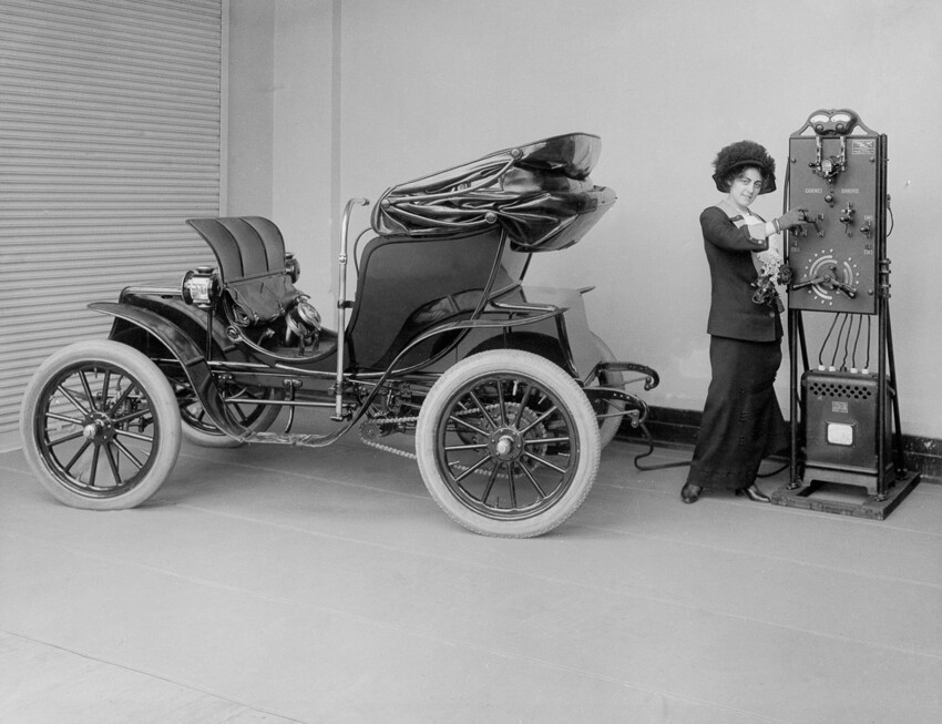 1912г. Женщина использует зарядное устройство с рукояткой для зарядки своего автомобиля Columbia Mark 68 Victoria. Автомобиль выпущен компанией Pope Manufacturing в 1906м, а зарядное устройство в 1912м.