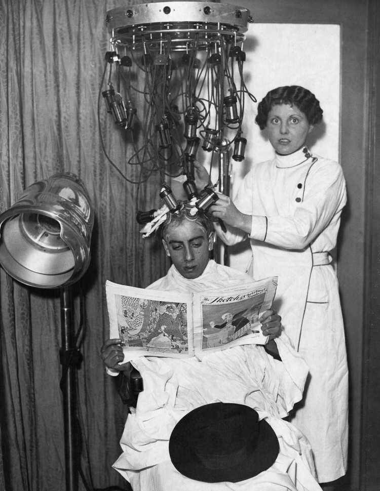 1935 г. Косметолог прикрепляет к голове мужчины трубки и подушечки машины для лечения волос.