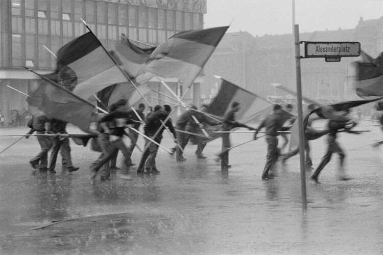 Молодые люди с немецкими флагами во время ливня на Александрплатц в Восточном Берлине