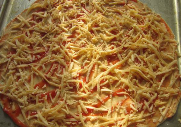 5. Натри сыр на крупной терке и слегка присыпь им тесто. Приправь орегано — эта специя придаст пицце душистого аромата.