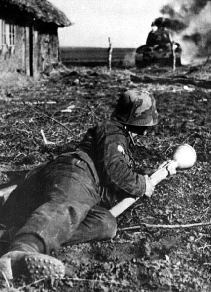 12. Пехотинец Ваффен СС с гранатомётом Панцерваффен в руках. На заднем плане горит советский Т-34. 1944-й год