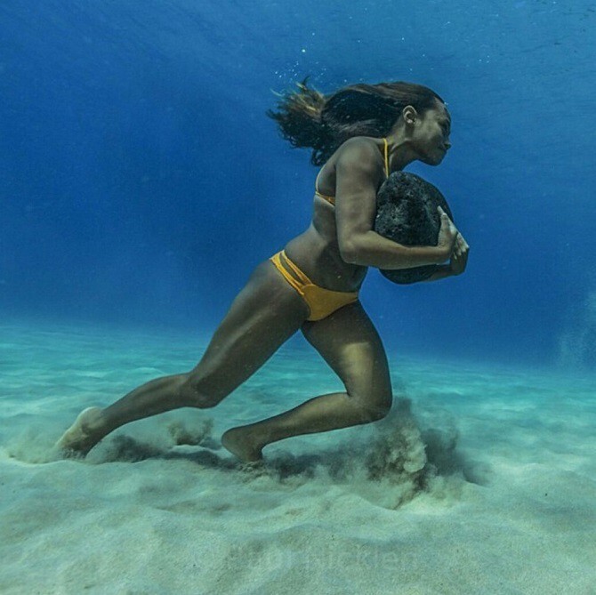 Серфингистка тренирует выносливость. Она бегает по дну океана с 20-килограммовым камнем, чтобы иметь силы противостоять ударам волн.