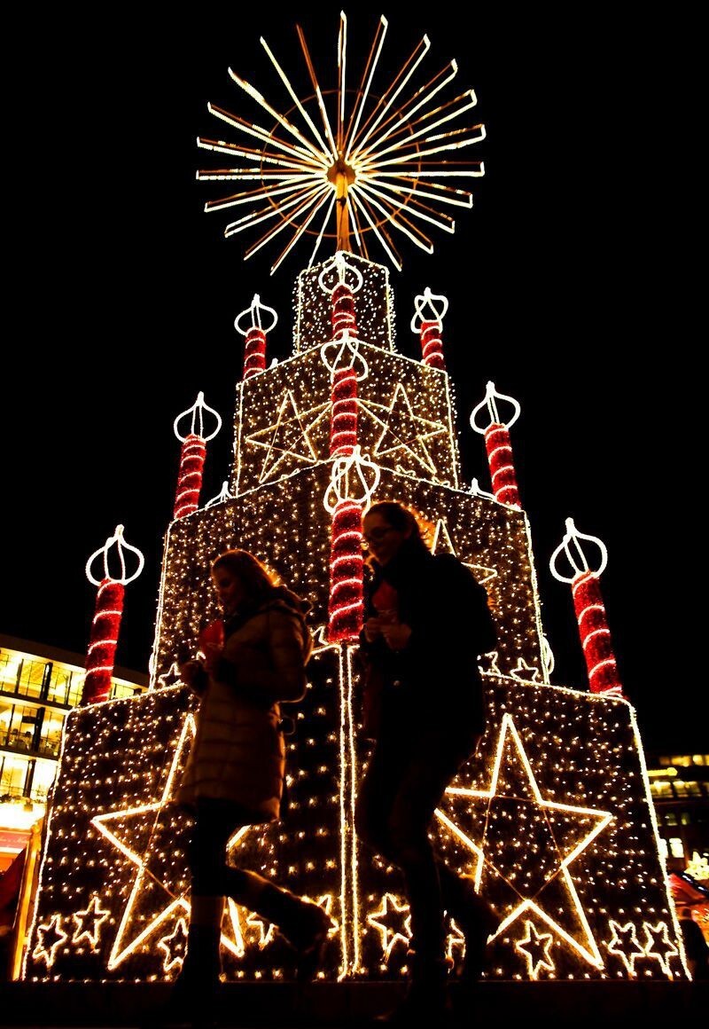 Две женщины надменно проходят перед ярким праздничным оформлением на рождественской ярмарке в Берлине.