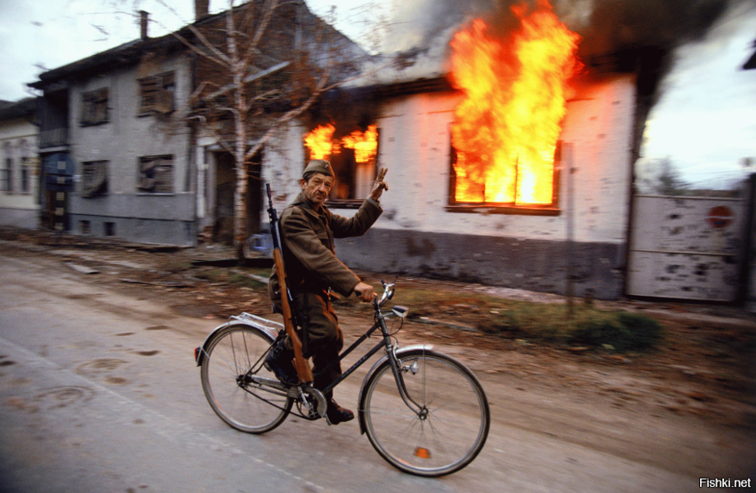 A Serbian soldier cycles by a burning house on the destroyed streets of the C...