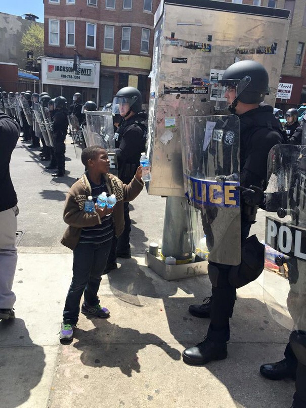 13. Мальчик предлагает воду полицейским в жаркий день во время протестов в Балтиморе