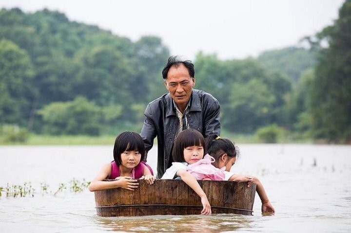 Отец в Китае везёт детей из школы во время наводнения.