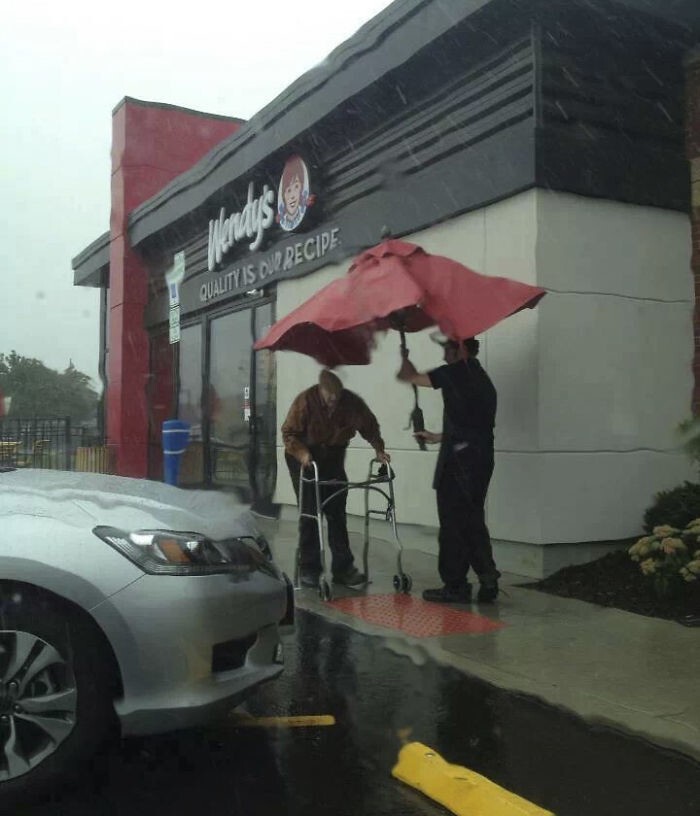 Сотрудник кафе взял уличный зонтик, стоявший над столом, чтобы помочь старику дойти до машины во время дождя