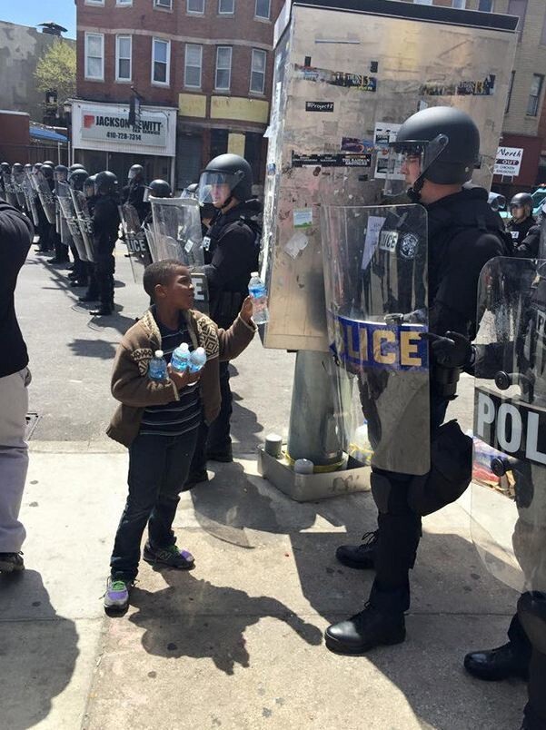 Мальчик предлагает воду полицейским в жаркий день во время протестов в Балтиморе