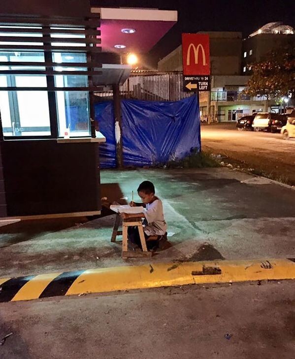 Бездомный мальчик делает уроки при свете от местного Макдональдса