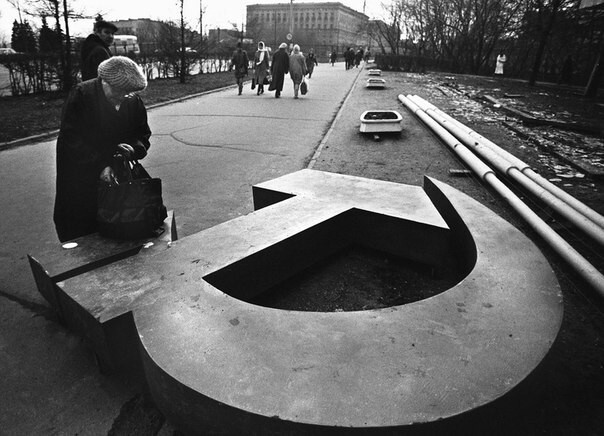 Женщина копается в сумке на поваленном серпе и молоте на улице в Москве, 1991 год  