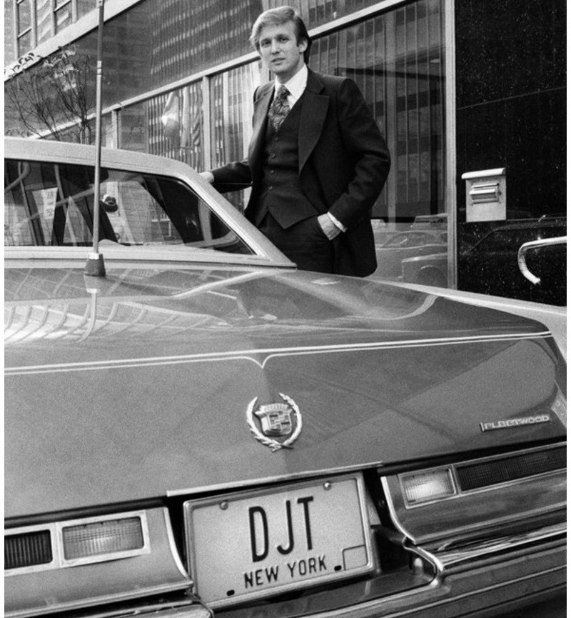 Дональд Трамп начинает день торговли недвижимостью, садясь в свой Cadillac – так подписали эту фотографию 1976 года в New York Times, где бизнесмен изображен с Cadillac Fleetwood Brougham (1976) с именными номерами-инициалами