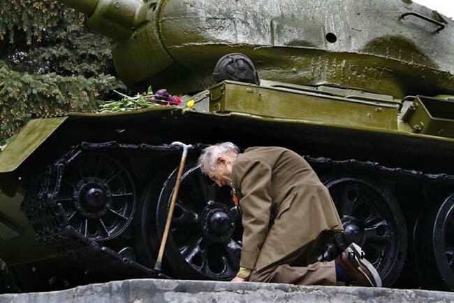 Советский ветеран стоит на коленях перед танком, в котором он прошел войну. Теперь это памятник