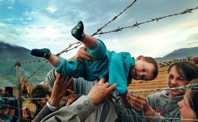 Маленького ребенка передают через колючую проволоку его бабушке и дедушке, которые находятся в лагере для беженцев, во время войны в Косово (2000 г.)