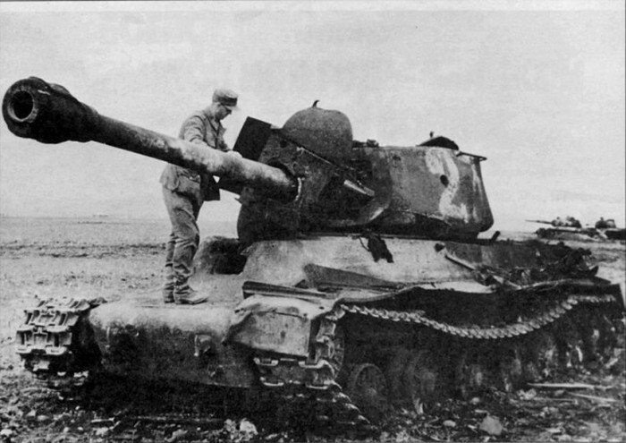 Немецкий солдат осматривает уничтоженный взрывом боекомплекта в результате пробития лобовой брони над люком механика-водителя советский танк ИС-2. На дальнем плане видны еще два подбитых ИСа. 