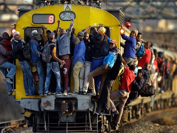 11. Пассажиры переполненного поезда в Соуэто, ЮАР, путешествуют, прицепившись к вагонам спереди и сбоку.