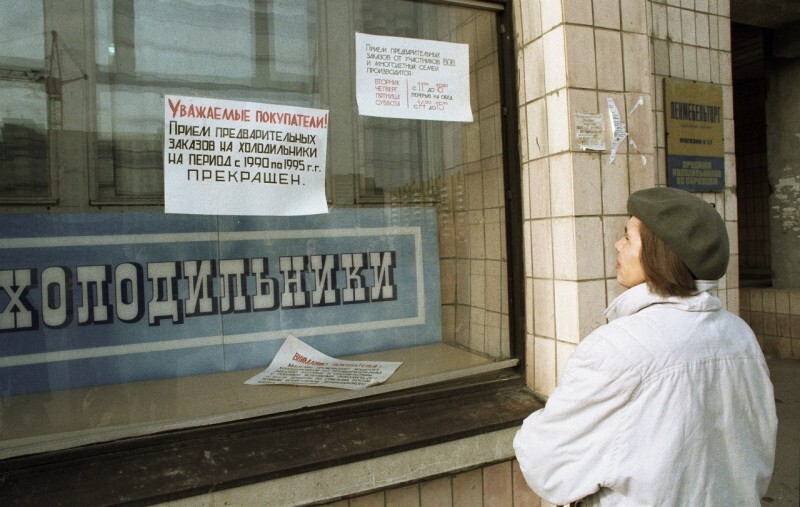 Женщина читает объявление в витрине магазина бытовой техники об отсутствии в продаже холодильников во время дефицита товаров в начале 90-х годов в СССР