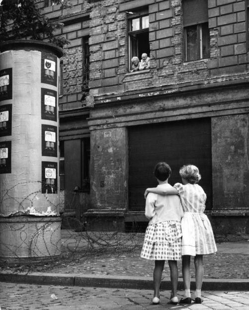 Две девочки на улице Западной Германии разговаривают со своими бабушкой и дедушкой в окне дома в восточной зоне, отделенной баррикадой из колючей проволоки, 14 августа 1961 года.