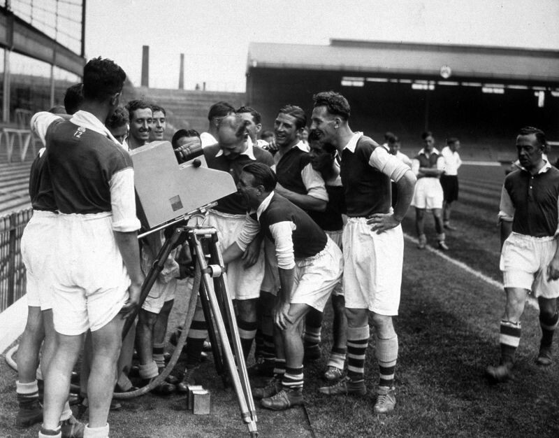 1937: Игроки Арсенала заглядывают в мгновенную телекамеру Marconi-EMI после первого в истории футбольного матча, который транслировали в прямом эфире.