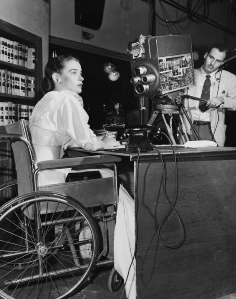 1951: Актриса Сьюзан Питерс сидит за столом в инвалидной коляске перед телекамерой WPTZ, транслирующей ее шоу «Мисс Сьюзан»