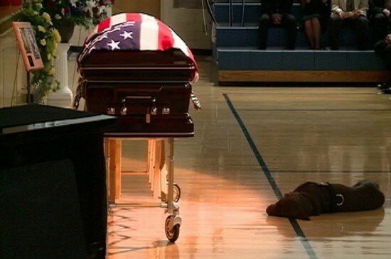Собака погибшего военного лежит у его гроба на похоронах в Рокфорде, штат Айова.