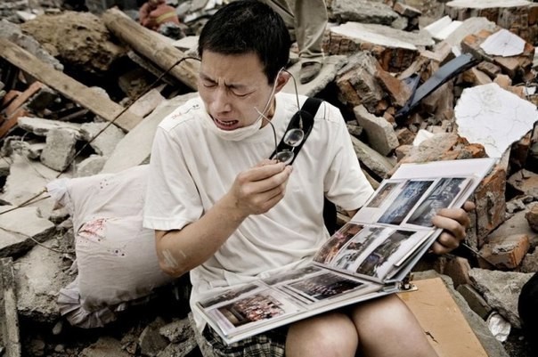Парень смотрит семейный альбом, найденный в руинах своего дома после землетрясения в Сычуани