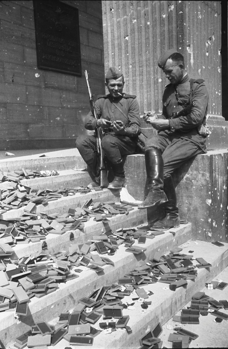 Советские солдаты сидят на ступенях разрушенного Рейхстага и рассматривают не врученные фашистские награды, 1945 год