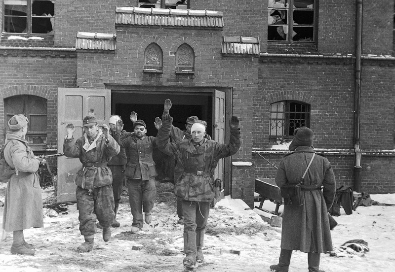 Пленные гитлеровцы выходят из дверей здания под конвоем советских бойцов.