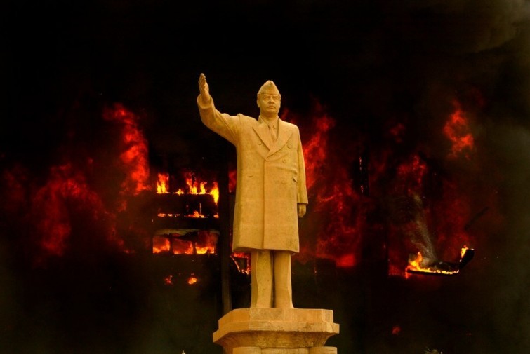  Статуя Саддама Хусейна на фоне горящего Национального олимпийского комитета Ирака во время бомбардировок ВВС США, 2003 год