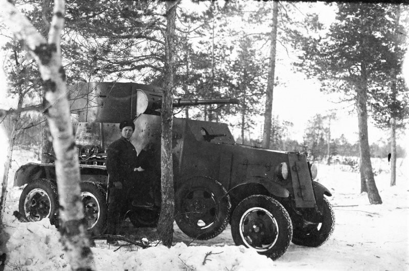 Красноармеец позирует на фоне бронеавтомобиля БА-6 в заснеженном перелеске.