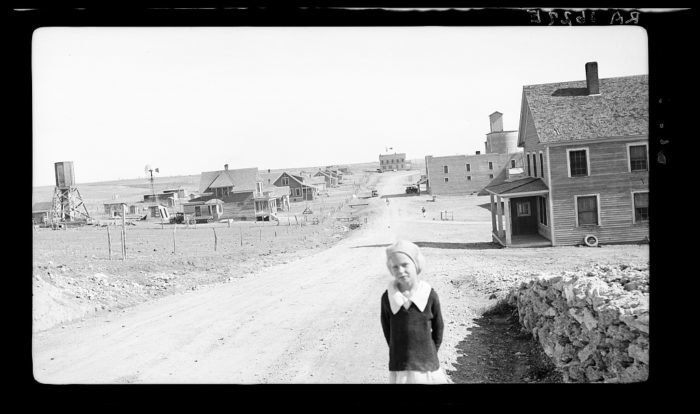 Девочка у дороги, ведущей к городку Миллс графства Хардинг. Фотограф отметила, что элеватор и городской банк были на тот момент закрыты из-за пыльных бурь и Великой Депрессии.